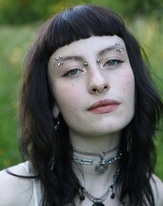 a woman with black hair and piercings on her nose is standing in the grass