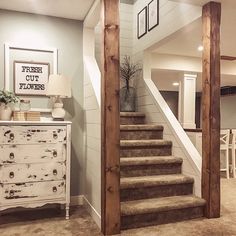 a staircase leading up to a living room with white furniture and pictures on the wall