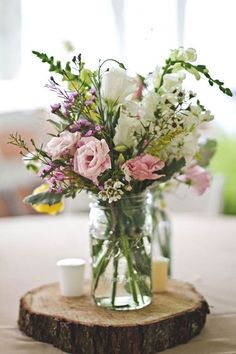 a vase filled with lots of flowers sitting on top of a wooden slice in front of a window