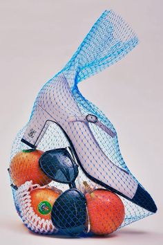 a bag filled with assorted fruit sitting on top of a white table next to a pair of scissors