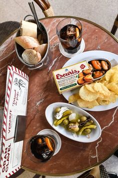 a table topped with plates of food next to bowls of chips and sauces on top of a glass table