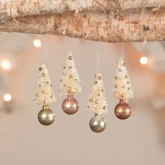 christmas ornaments hanging from a branch with lights in the background