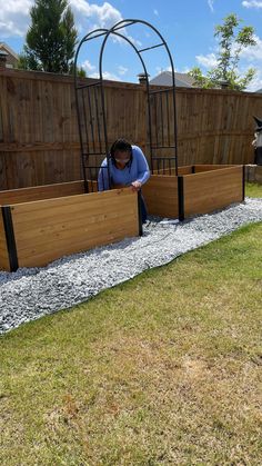 a man is working on some wooden planters in the yard with gravel and grass