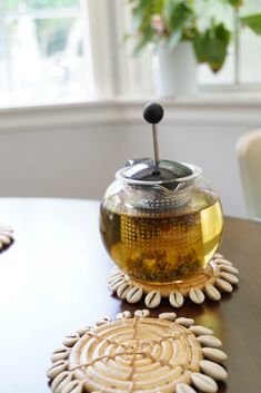 a tea pot sitting on top of a wooden table next to two coasters with flowers