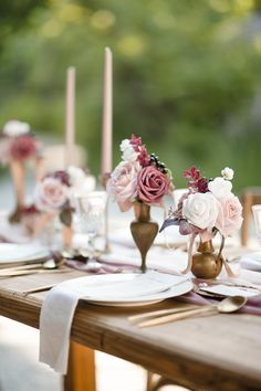 the table is set with pink and white flowers in vases, napkins, and candles