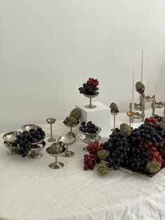 a table topped with lots of different types of fruits and silver dishes filled with grapes