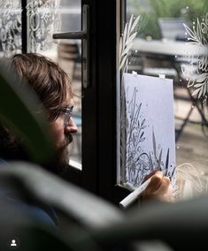 a man is looking out the window while drawing on paper with an easel in front of him