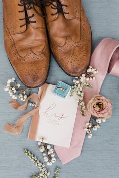 a pair of brown shoes sitting on top of a table next to a pink ribbon