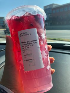 a person holding up a plastic cup filled with liquid in front of a car window