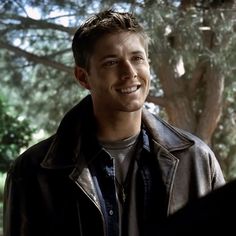 a smiling young man standing in front of a tree