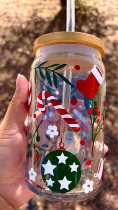 a hand holding up a glass with christmas decorations on it and a straw in the bottom