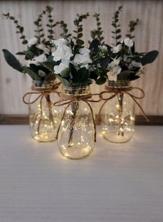 three mason jar vases with flowers and string lights on the lids are sitting on a table