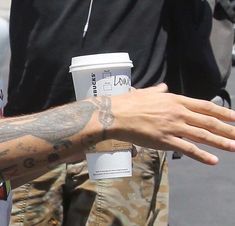 a man with tattoos on his arm holding a coffee cup