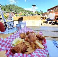 a basket filled with fried fish and fries on top of a table next to a drink