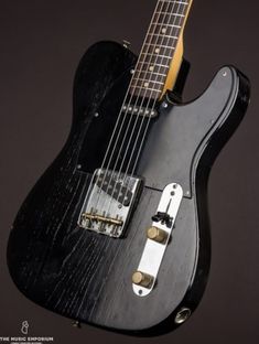 an electric guitar with a black body and gold hardware on it's neck, against a dark background