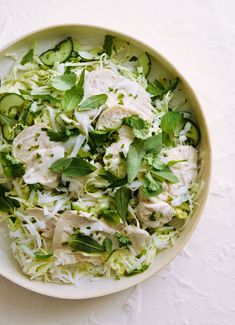 a white bowl filled with shaved cabbage and chicken salad on top of a wooden table