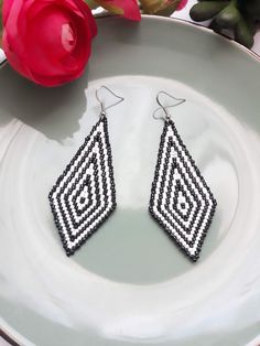 a pair of black and white beaded earrings sitting on top of a plate next to a red rose