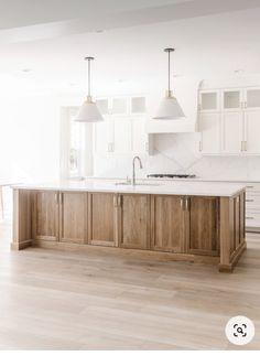 an empty kitchen with white cabinets and wooden flooring is pictured in this image, there are two pendant lights hanging over the island