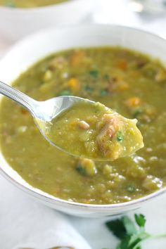 a spoon full of green soup on top of a white plate with another bowl in the background