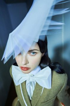 a woman with black hair wearing a suit and white bow tie in front of her head