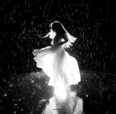 a woman standing in the rain wearing a white dress and holding an umbrella with her hands