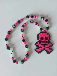 a pink and black beaded pacman necklace next to it's matching bracelet