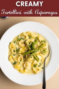 a white bowl filled with pasta and asparagus on top of a wooden table