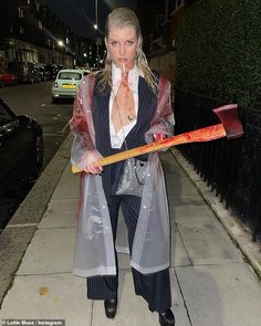 a woman dressed up as a zombie holding an ax in her hand and wearing a plastic coat