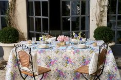 the table is set for two outside with flowers on it and plates in front of them