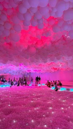 many people are standing under balloons floating in the air at an art installation with pink and blue lighting