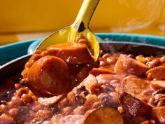 a ladle full of beans and sausage being spooned into a pot filled with stew