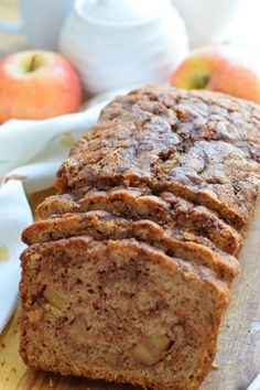 two slices of banana bread sitting on top of a wooden cutting board next to apples