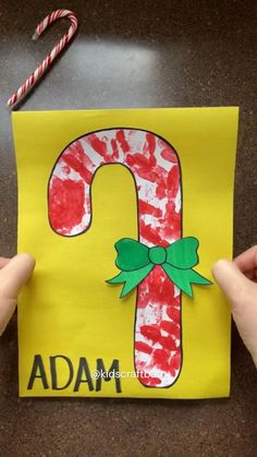 two hands holding up a piece of paper with the letter j on it and candy canes next to it