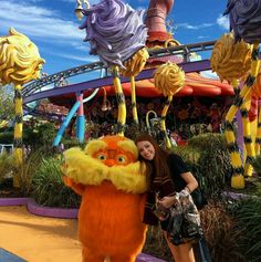 a woman standing next to a giant stuffed animal in front of a roller coaster at a theme park