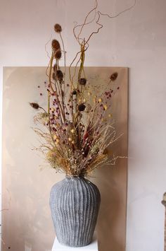 a vase filled with dried flowers sitting on top of a white table next to a painting