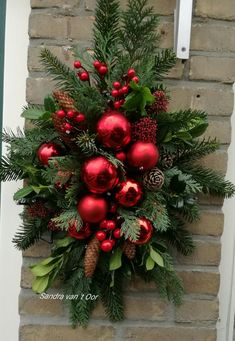 a christmas wreath hanging on the side of a building with red ornaments and pine cones