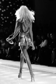 a woman is walking down the runway in a short skirt and high heeled shoes