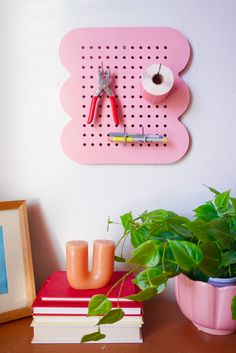 a pink peg board mounted to the side of a wall next to a potted plant