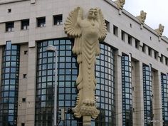 an angel statue in front of a building with many windows on the side and below it