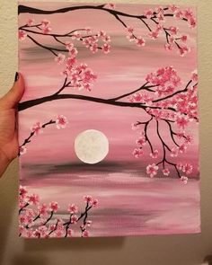 a person is holding up a painting with pink flowers and a full moon in the background