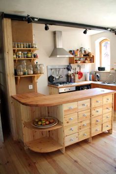 a kitchen with an island and shelves filled with food on top of wooden flooring