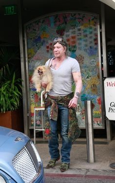 a man walking down the street with a dog in his hand and another car parked next to him