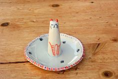 a small white plate with an orange and black cat on it's top sitting on a wooden table