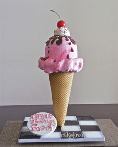 an ice cream cone with pink icing and a cherry on top, sitting on a checkered coaster