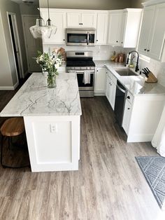 a kitchen with white cabinets and an island in the middle, surrounded by wood flooring