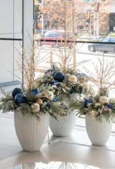 three white vases filled with blue and gold flowers on a table in front of a window