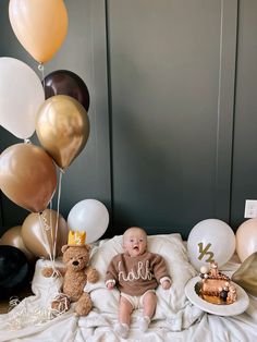 a baby is sitting on a blanket with balloons and other items in front of him