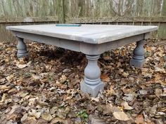 an old table sitting in the middle of leaves on the ground next to a fence