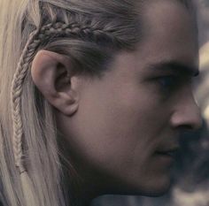 a man with long blonde hair and braids in his ears is staring into the distance