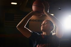 a woman holding a basketball up to her head in the air with light shining on her